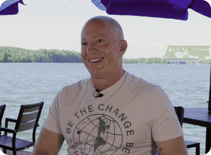 Amir Harpaz - the owner of The Mudpuppy, seated on a lakeside patio under blue umbrellas.