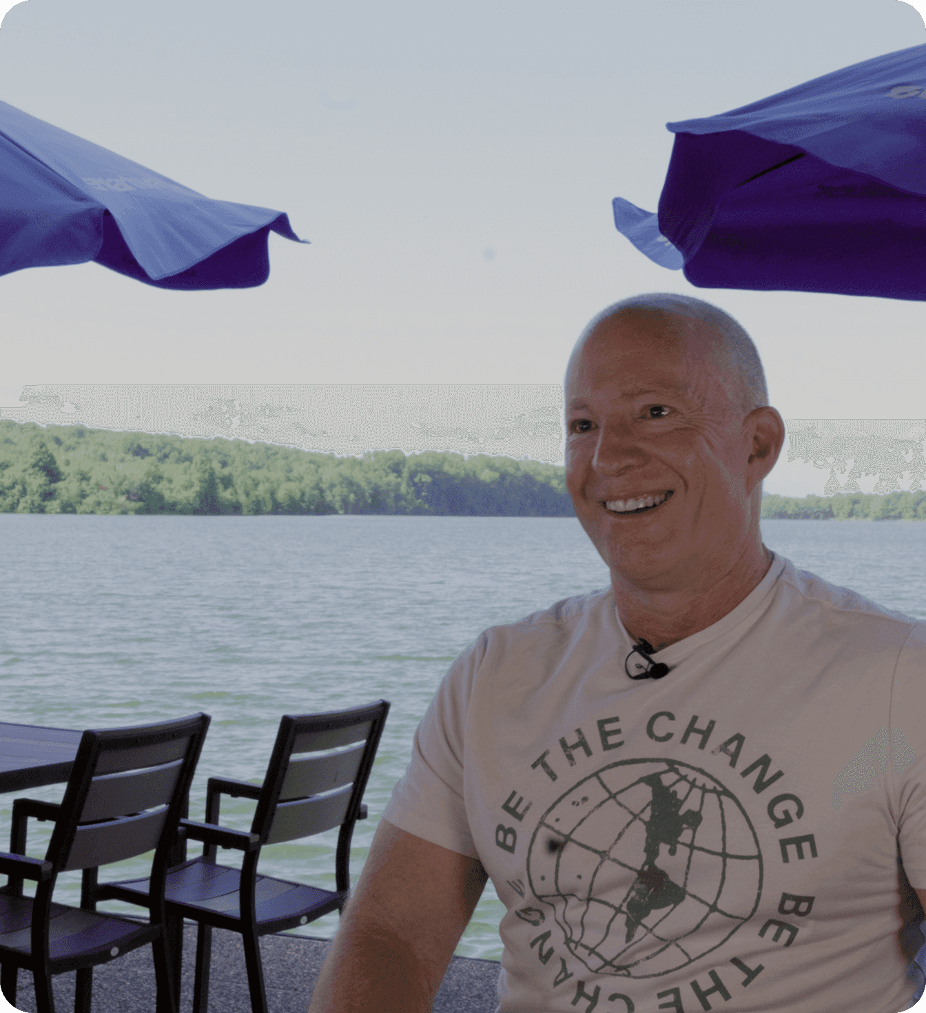 Amir Harpaz - the owner of The Mudpuppy, seated on a lakeside patio under blue umbrellas.