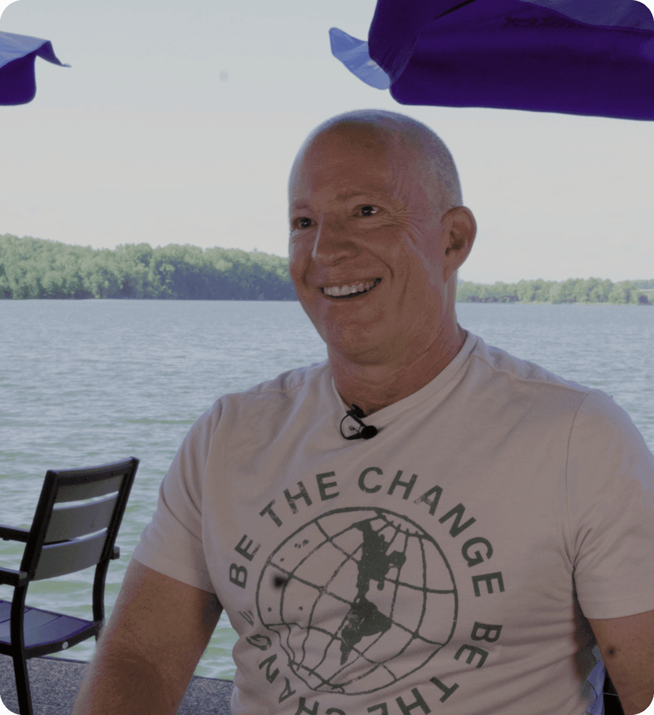 Amir Harpaz - the owner of The Mudpuppy, seated on a lakeside patio under blue umbrellas.