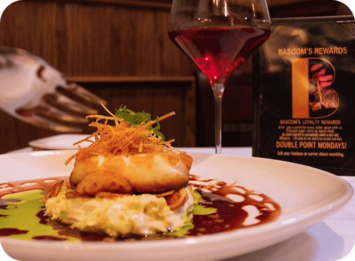 A plated seafood entrée and glass of wine beside a Bascom’s Rewards loyalty card on the table