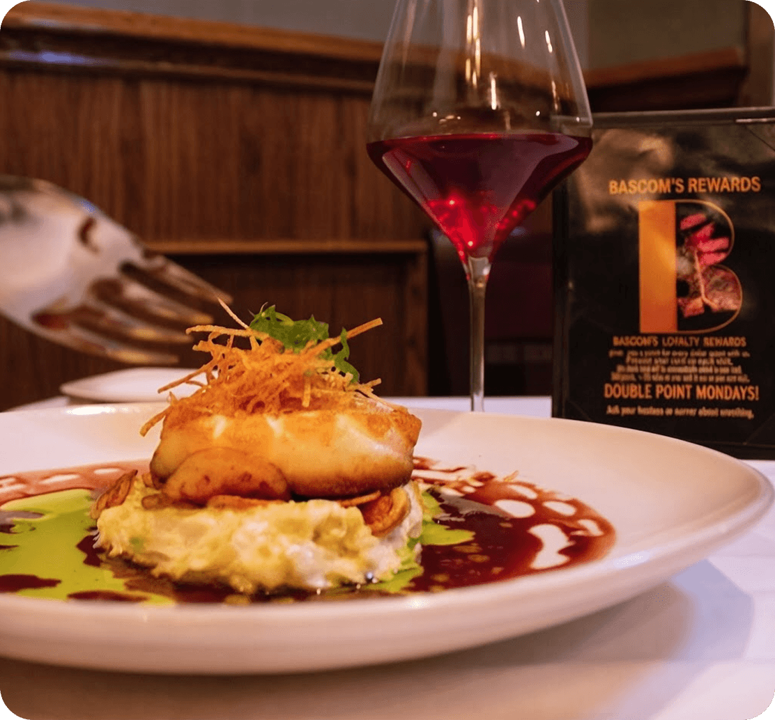 A plated seafood entrée and glass of wine beside a Bascom’s Rewards loyalty card on the table