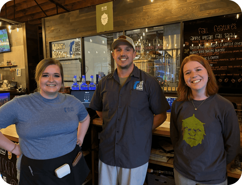 Three Big Lake Brewing team members smiling in front of the bar