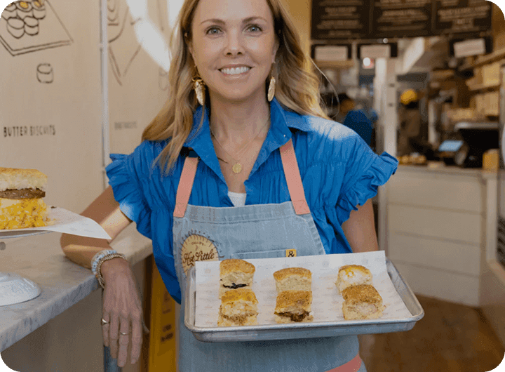 Callie’s Hot Little Biscuit founder holding tray of fresh biscuits in shop