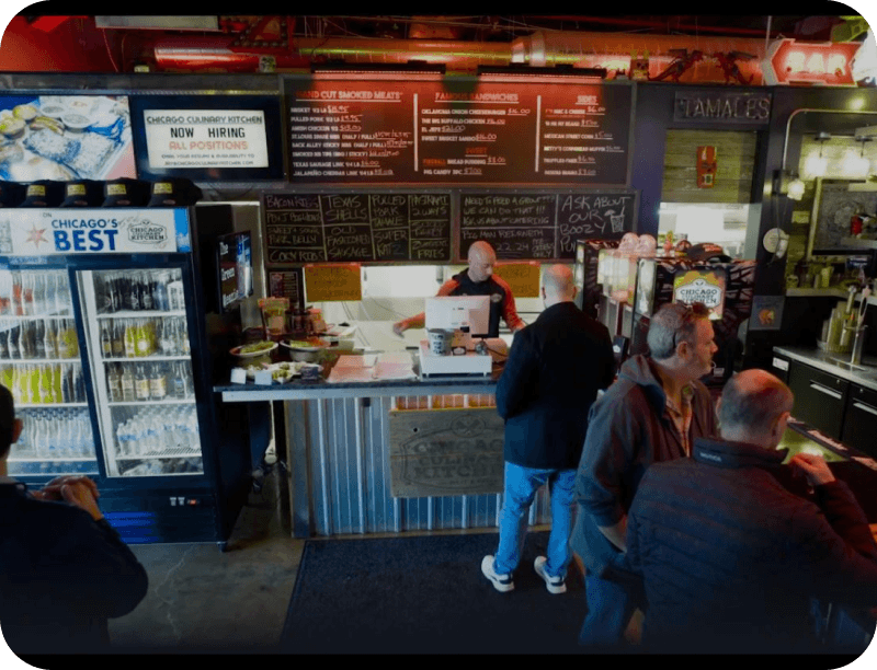 Guests ordering at the counter at Chicago Culinary Kitchen, with the full menu board and a “Now Hiring” sign behind the register