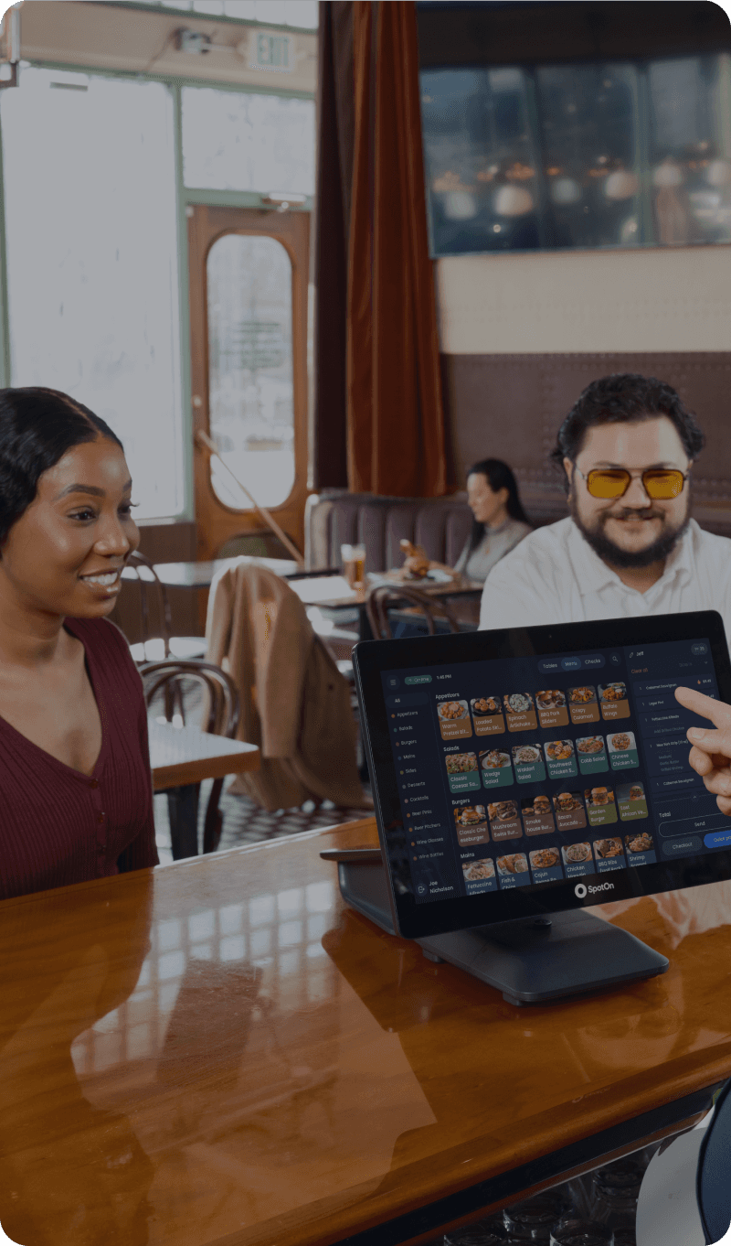 Cashier using POS system to assist smiling customers in a modern fast-casual restaurant.
