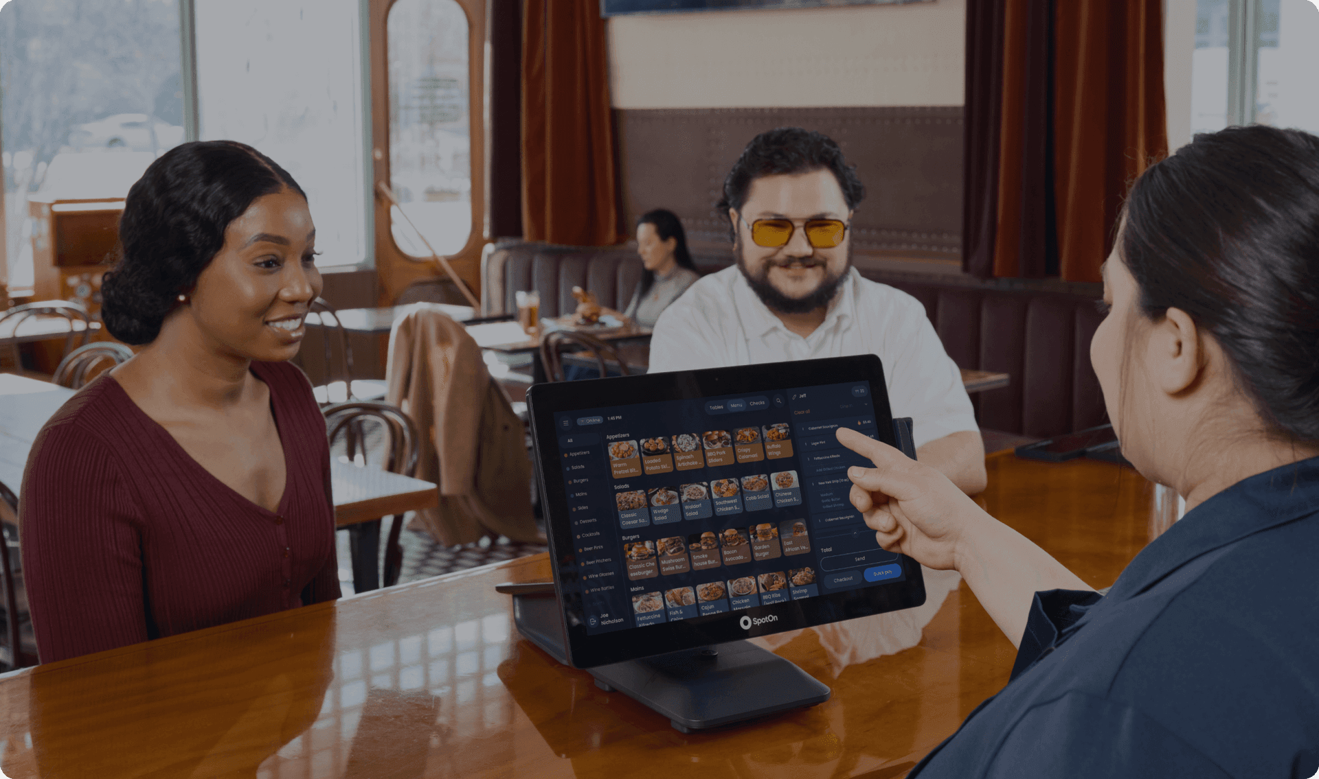 Cashier using POS system to assist smiling customers in a modern fast-casual restaurant.