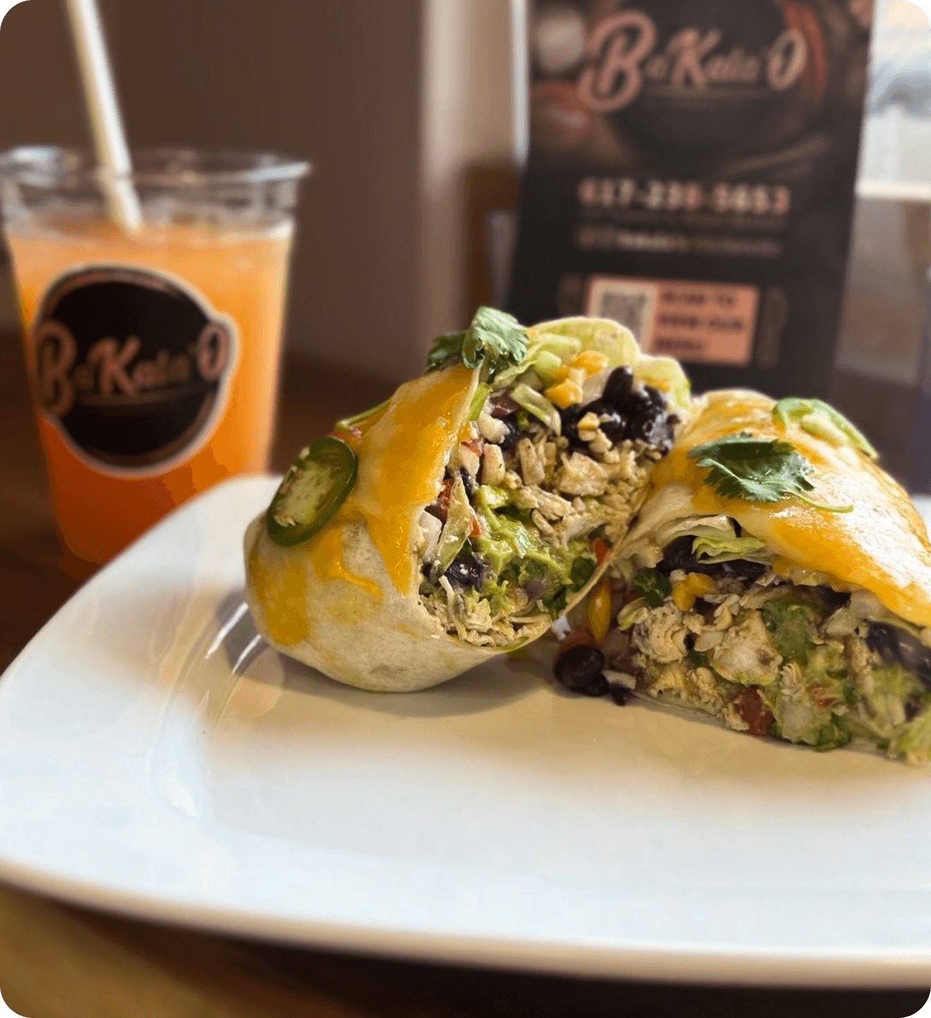 Burrito cut in half on a plate with a fresh drink beside it at a restaurant.
