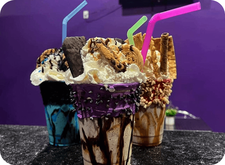 Colorful milkshakes topped with cookies, whipped cream, and chocolate drizzle