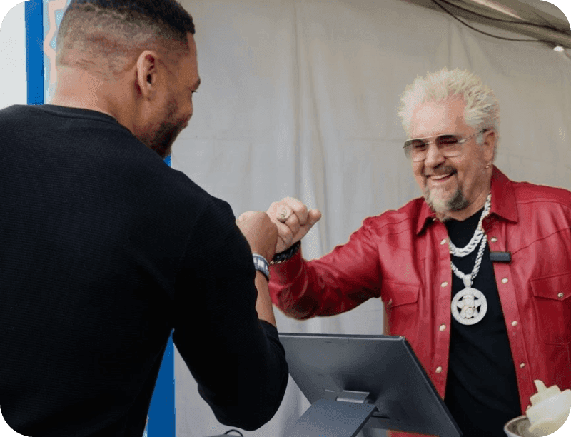 Guy Fieri fist-bumping a vendor at a SpotOn POS station at Guy’s Flavortown Tailgate