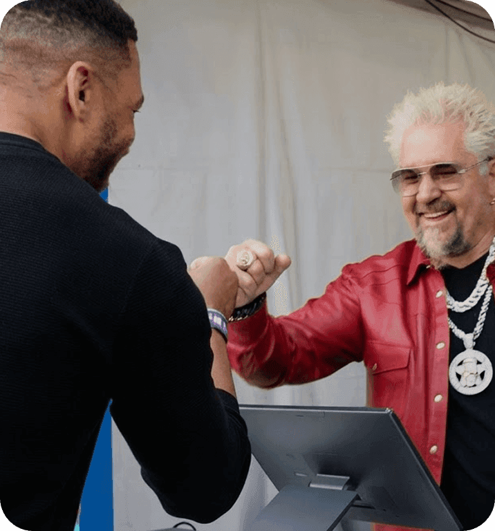 Guy Fieri fist-bumping a vendor at a SpotOn POS station at Guy’s Flavortown Tailgate