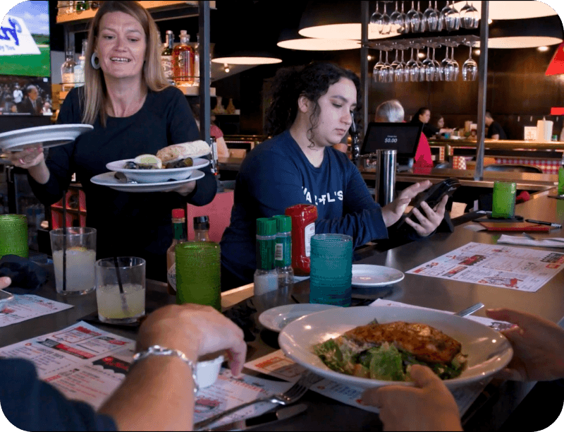 A server delivering plates of food to guests seated at the bar at Hazel’s