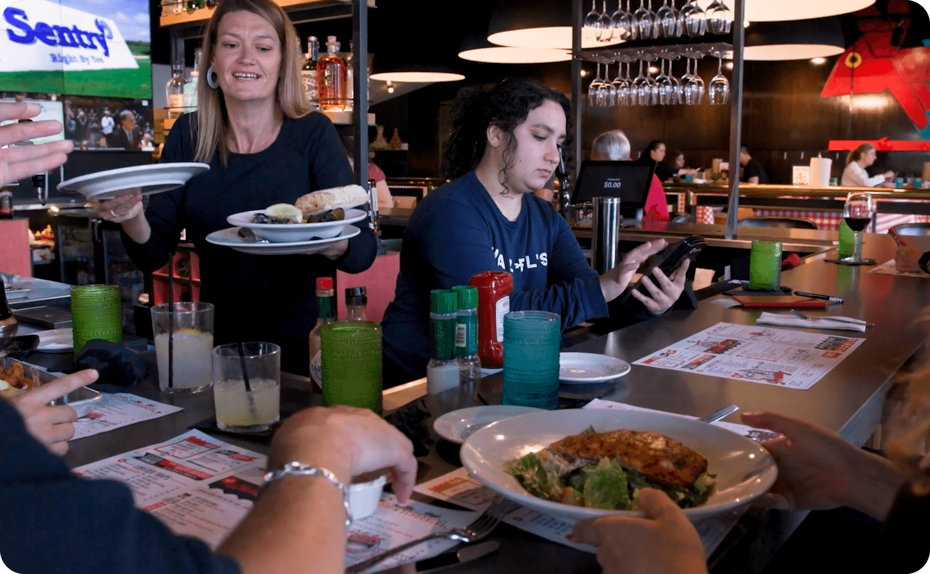 A server delivering plates of food to guests seated at the bar at Hazel’s