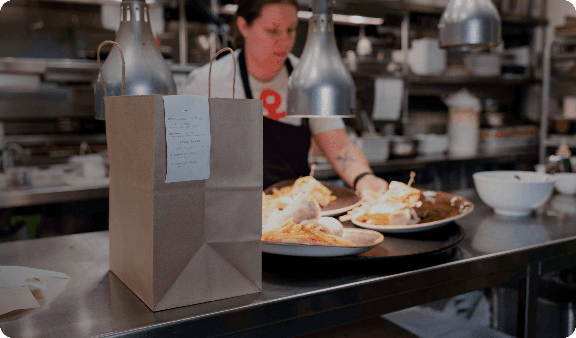 Takeout bag on kitchen counter as staff prepares plated food