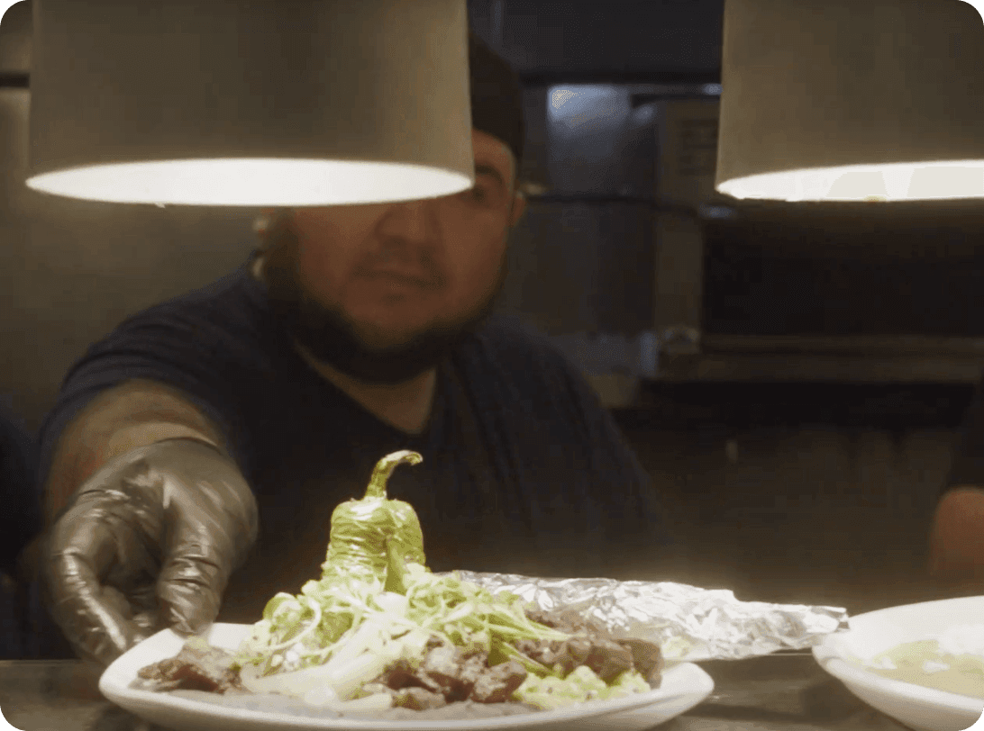 Restaurant dish presentation with fresh lettuce and a whole green pepper garnish being plated by server wearing food safety gloves