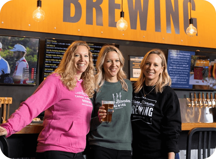 Three Blondes Brewing owners standing behind bar inside brewery taproom