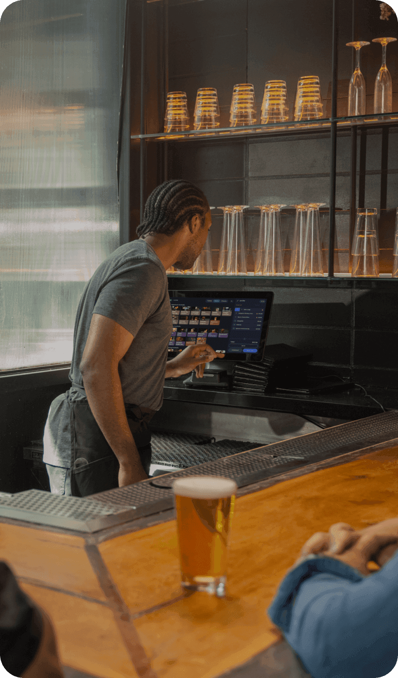 Bartender mixing a drink while serving a guest at a busy bar