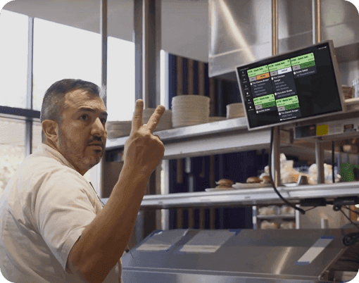 A chef in a kitchen holding up two fingers in front of SpotOn KDS