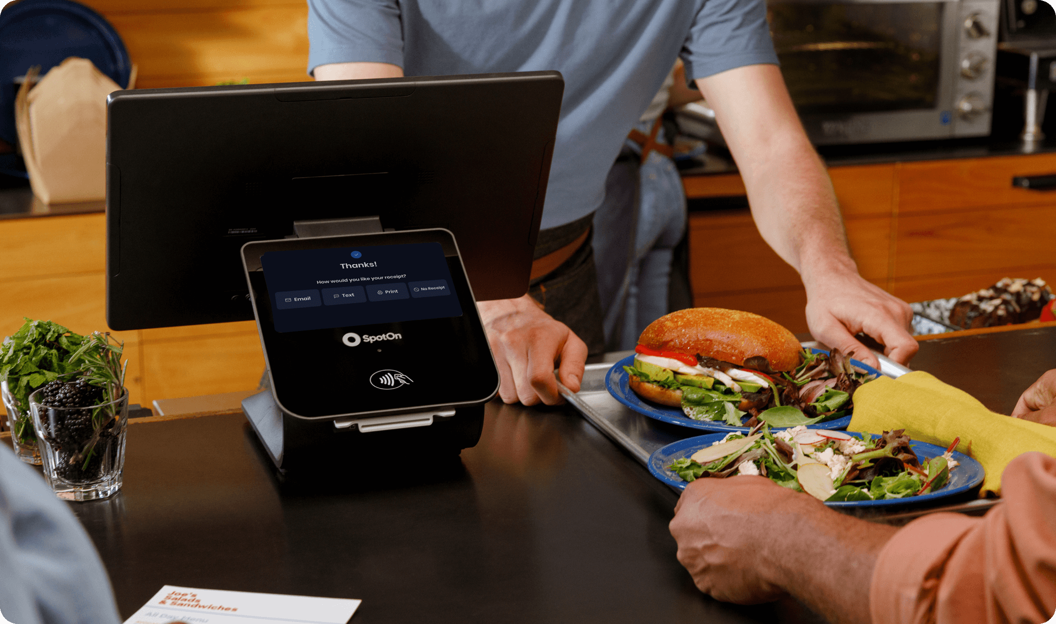 Restaurant staff using SpotOn POS at a counter-service restaurant to process an order with sandwiches and salads