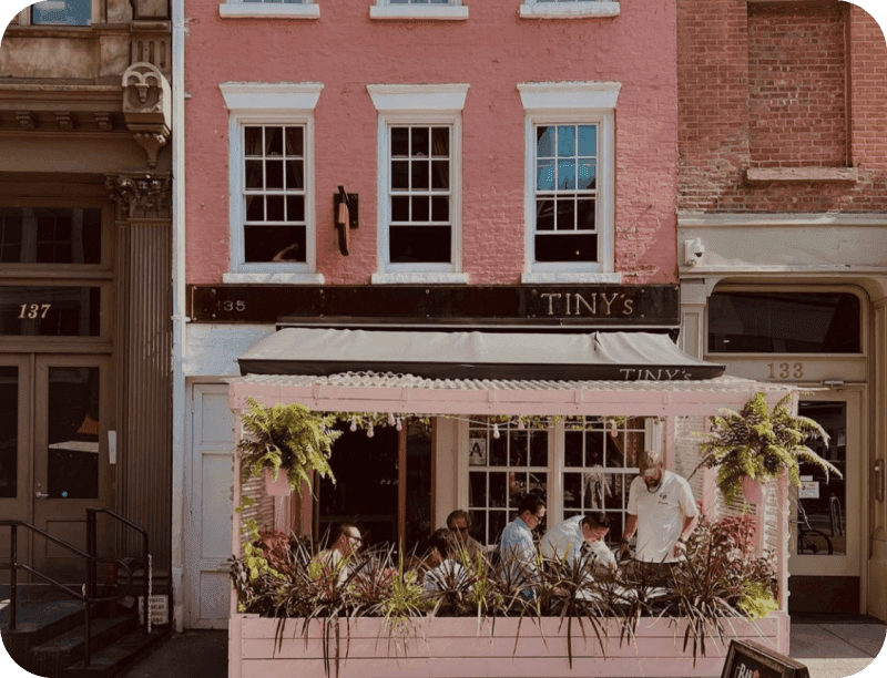 The pink townhouse exterior of Tiny’s & The Bar Upstairs, with guests dining on the covered patio