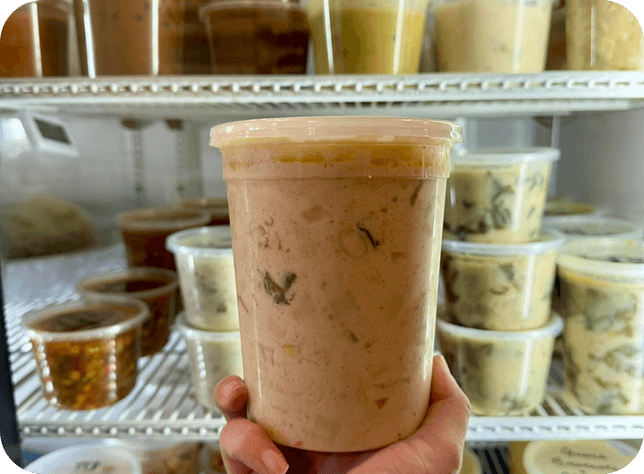 A container of soup held up in front of the grab-and-go cooler at Soup’d Up