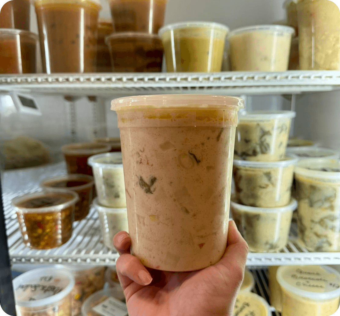 A container of soup held up in front of the grab-and-go cooler at Soup’d Up