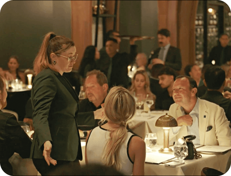 A staff member attending to a table of guests in the packed dining room at Adalina Prime