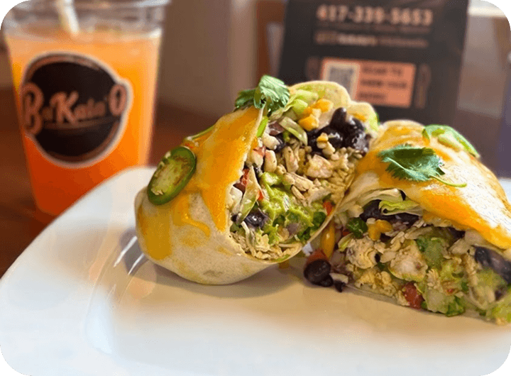 Fresh burrito halves on a plate beside a refreshing drink in a restaurant