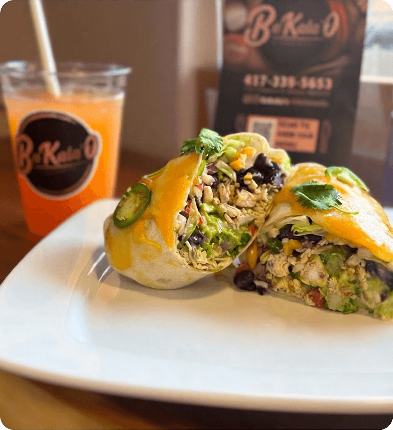 Fresh burrito halves on a plate beside a refreshing drink in a restaurant