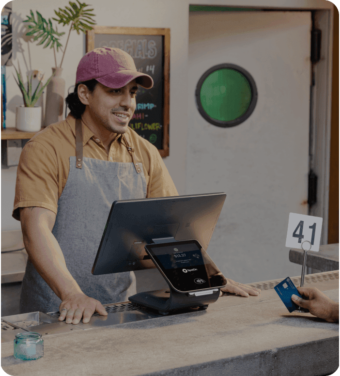 Restaurant cashier at counter using SpotOn POS system while a customer pays with a credit card.