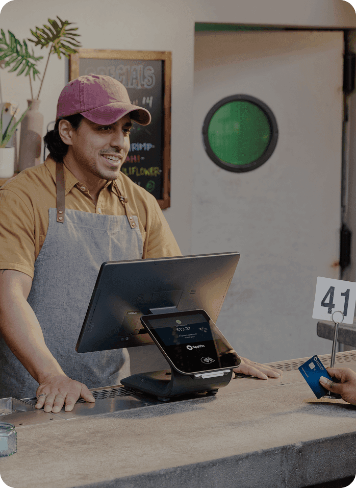 Restaurant cashier at counter using SpotOn POS system while a customer pays with a credit card.
