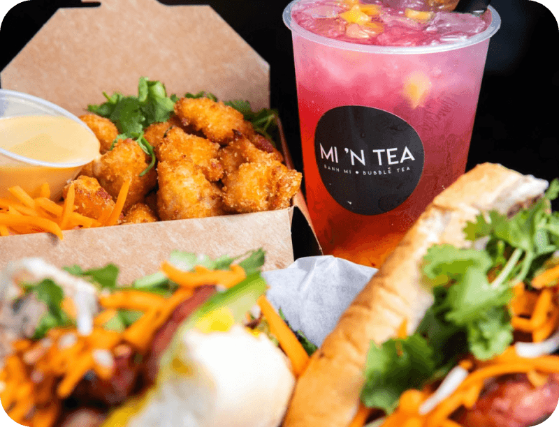 Bánh mì sandwiches, fried bites, and a pink bubble tea in a branded Mi ’N Tea cup
