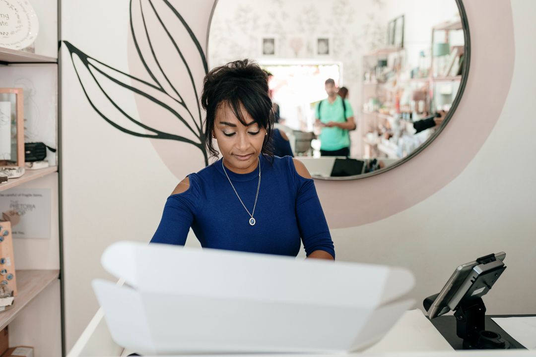 Retail boutique owner preparing a delivery box at the counter.