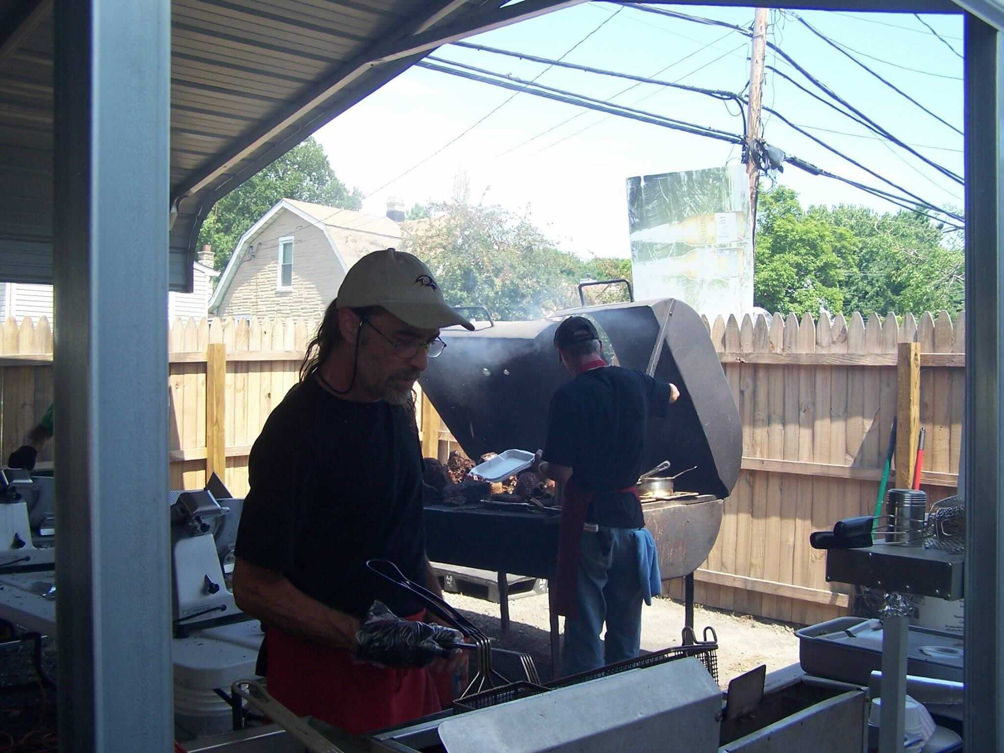 Two cooks prep food over an outdoor barbecue and fryer.