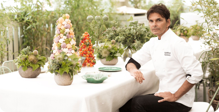 Chef Matthew Kenney sitting at an outdoor table with a white tablecloth and plants.