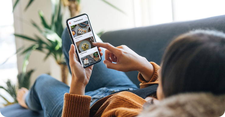 Woman lying on a couch ordering from an online menu on her phone.  