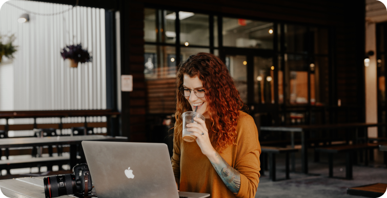 Woman working on a computer at a restaurant with a drink.