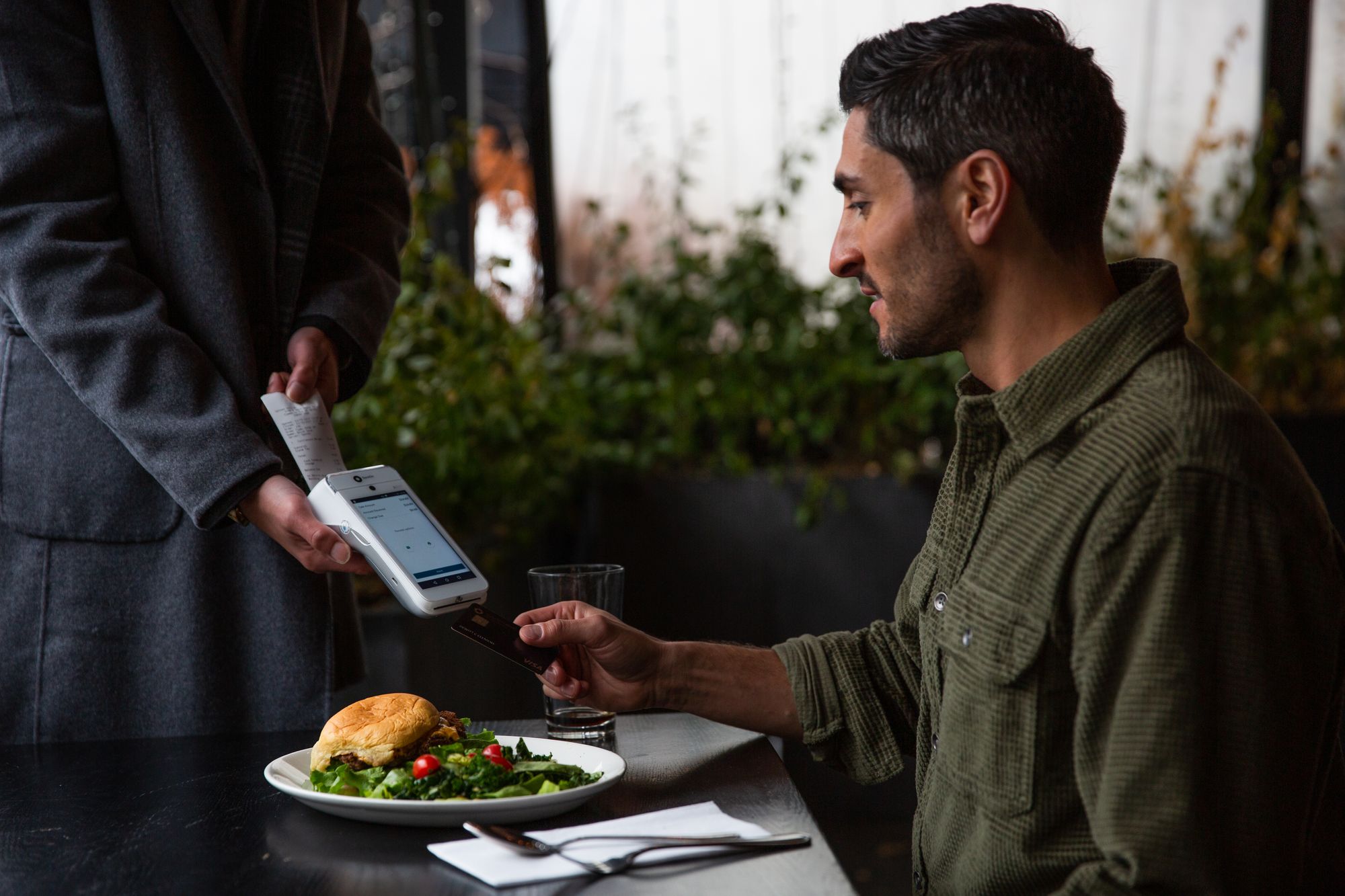 A restaurant server holds a handheld device for a guest to pay at the table.