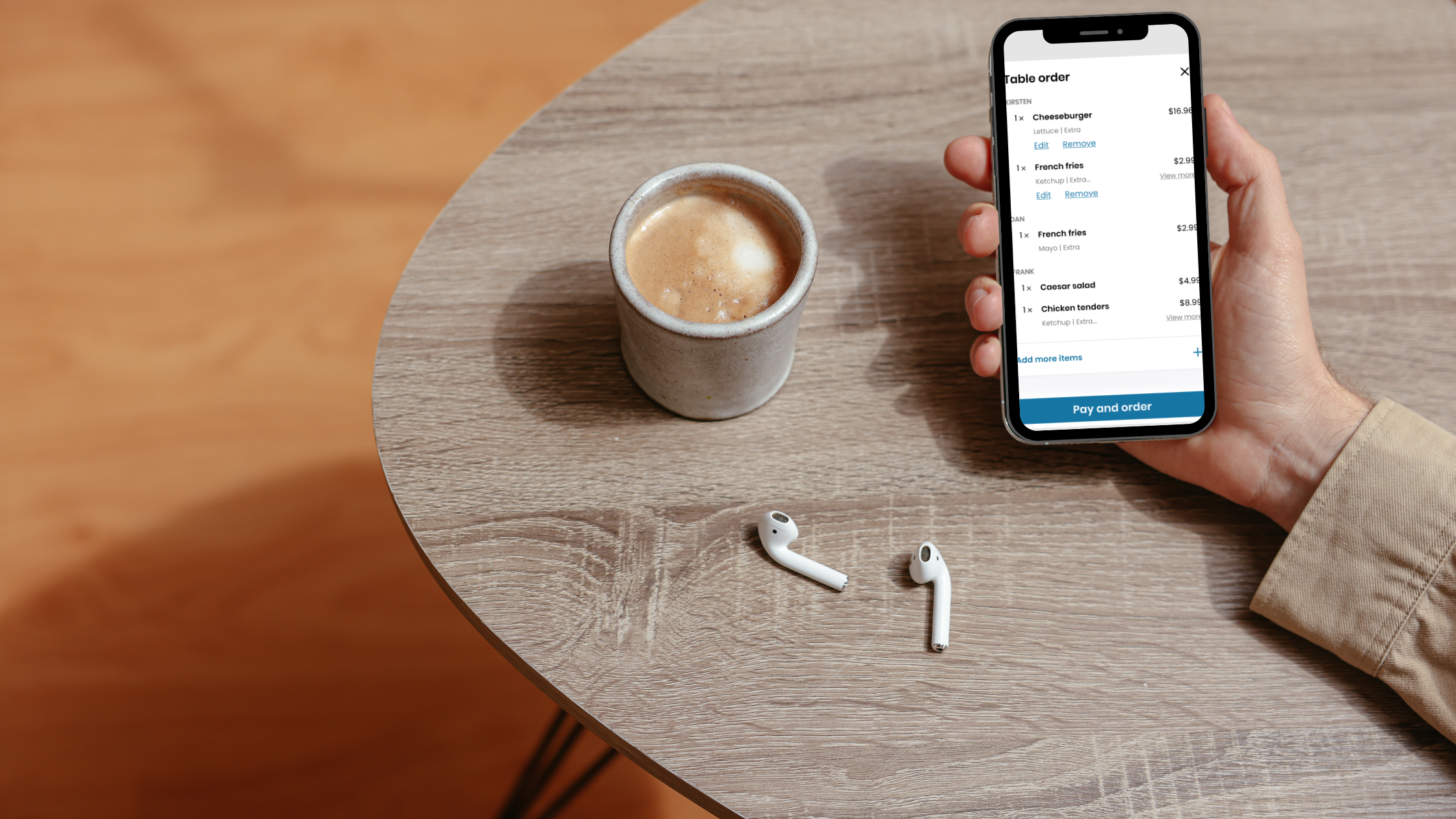 A hand holds an iPhone next to a cup of coffee and wireless headphones.