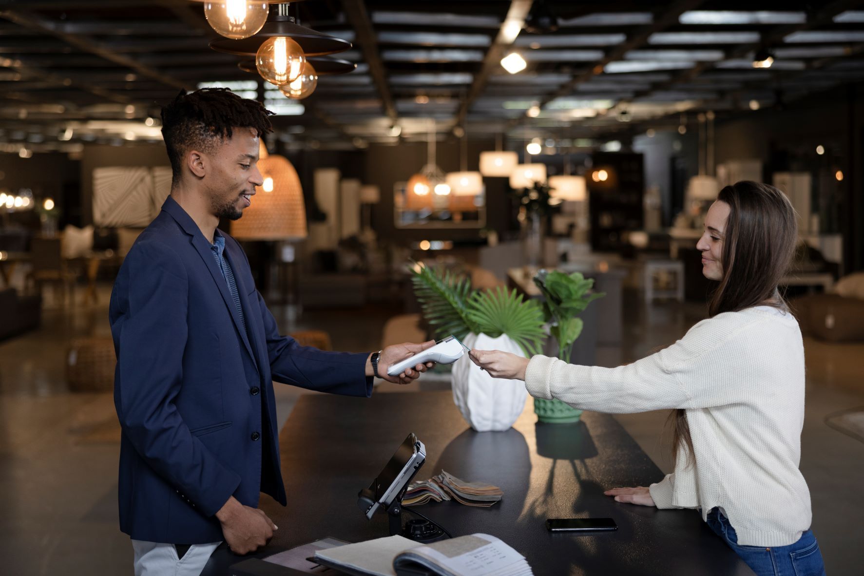 A retail employee holds the payment terminal up so the customer can tap their card to pay.