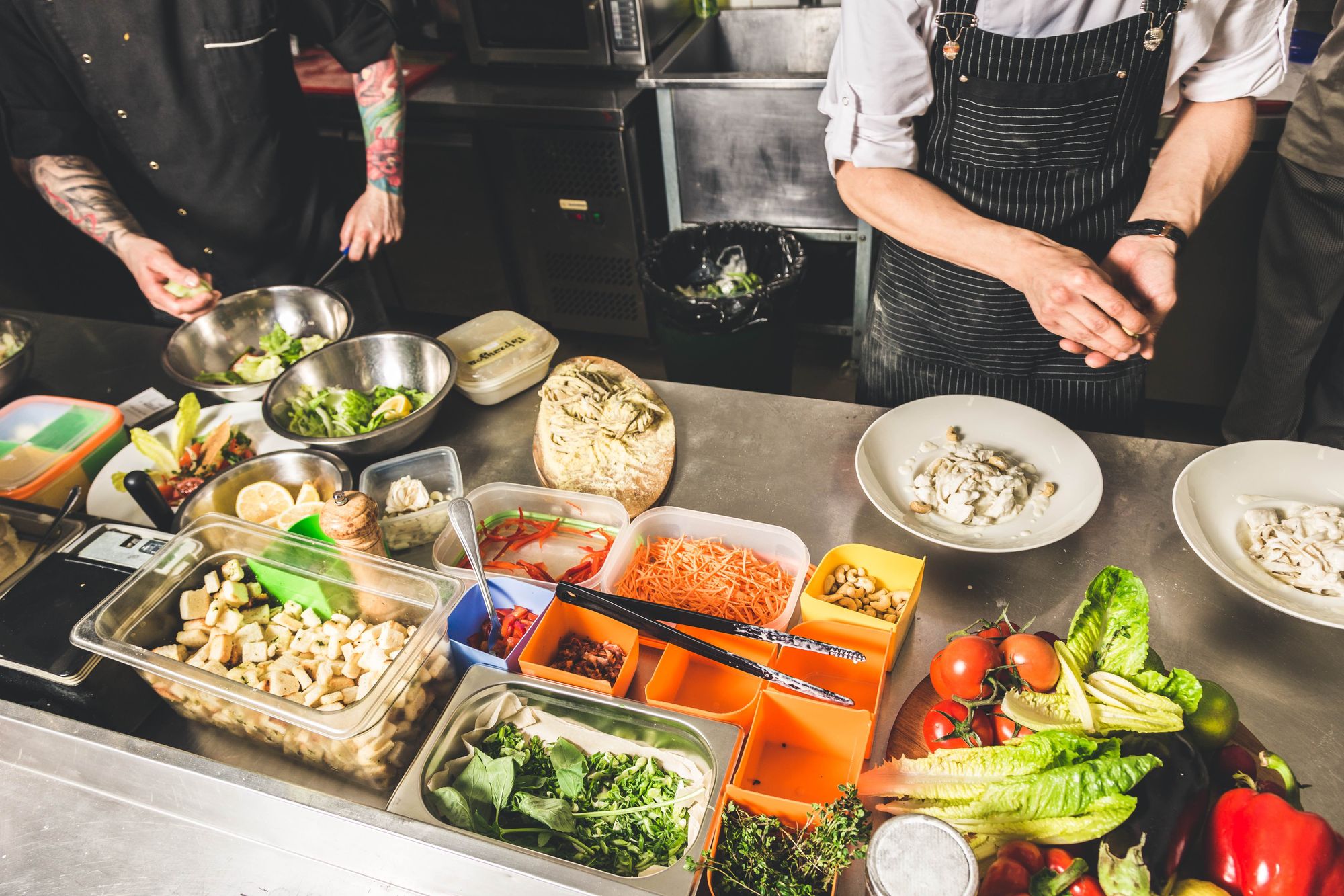 Chefs in the kitchen testing out menu items with several ingredients on the counter.