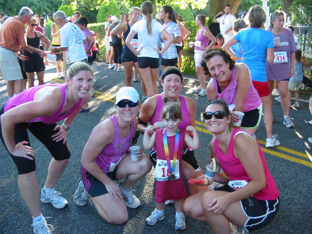 A child wearing a medal is surrounded by woman in athletic wear.