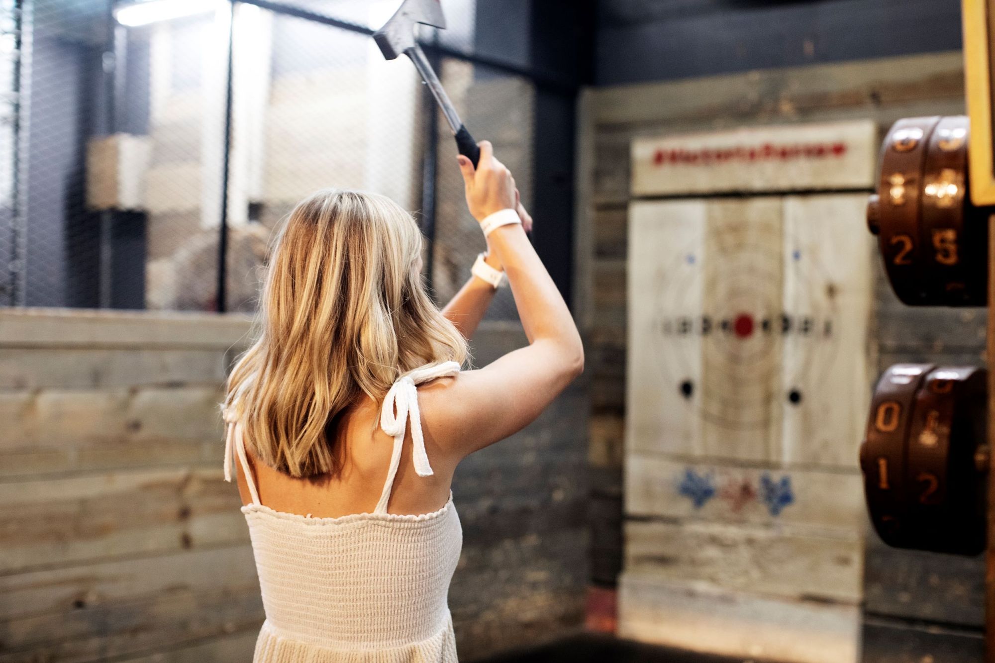 A woman holds an axe in the air before throwing it at a target