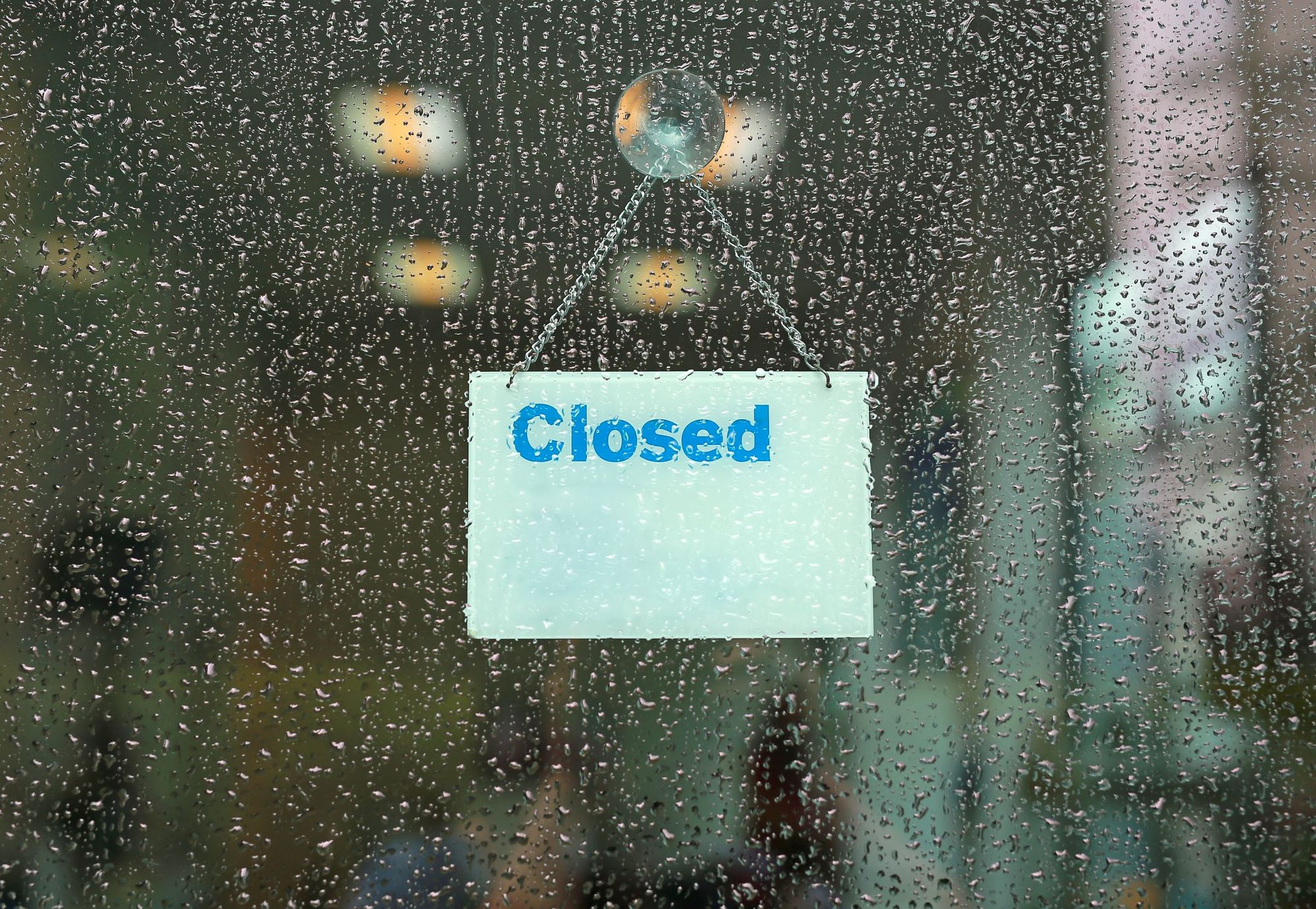 A shop window covered in rain drops with a closed sign