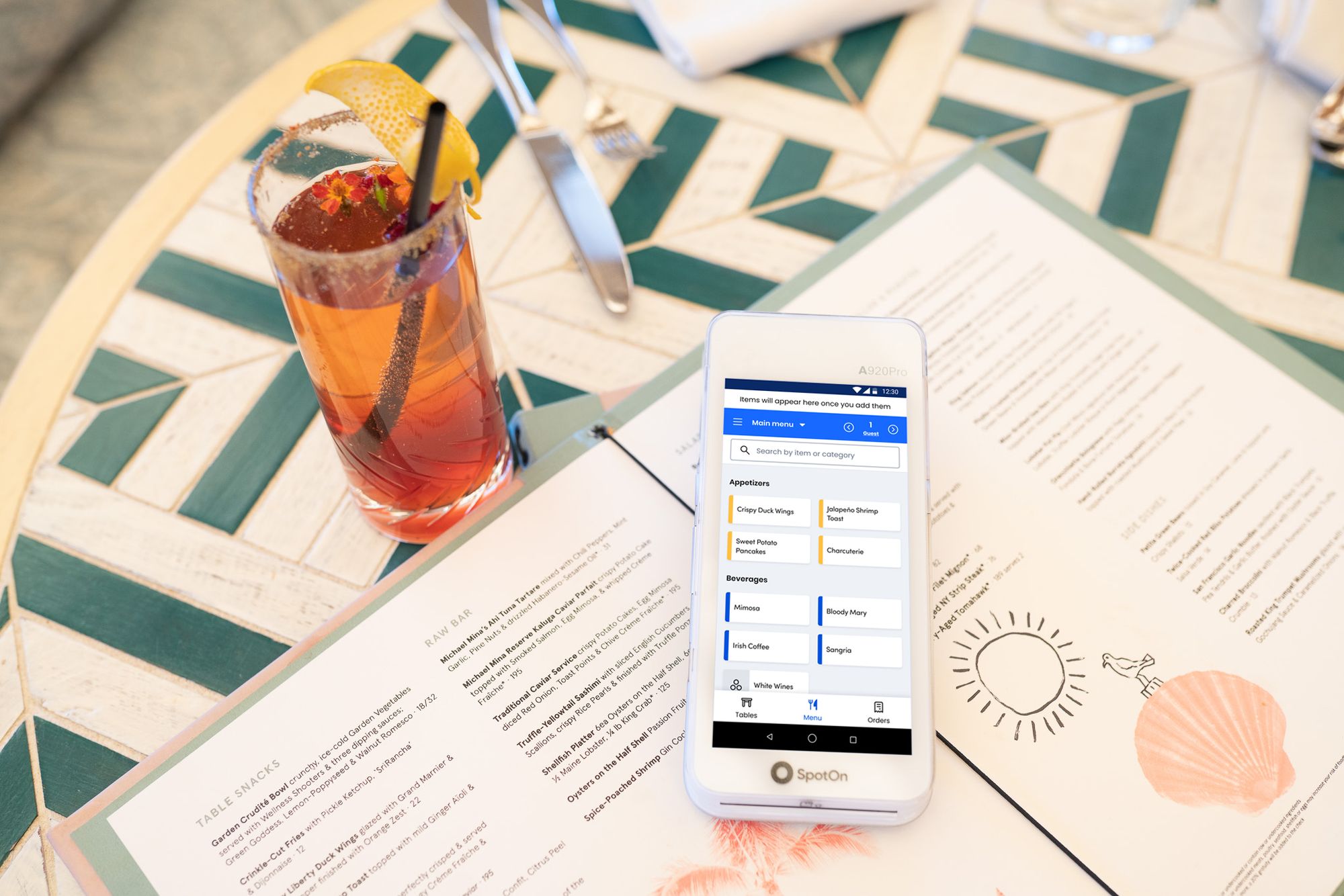 A small handheld point-of-sale device sits on a menu next to a glass of ice tea.