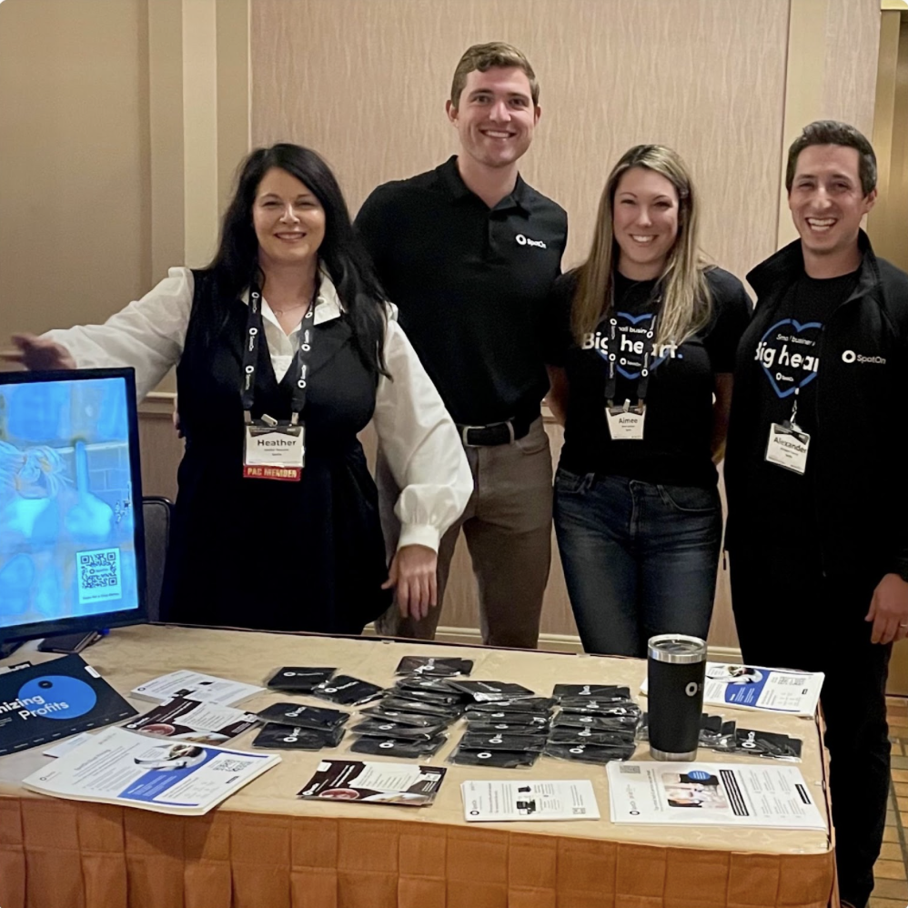 Four people pose and smile in front of a table with SpotOn merchandise.