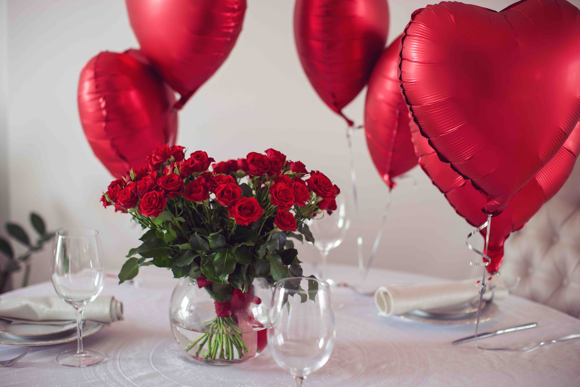 Table with a white tablecloth, red roses, and heart shaped balloons.