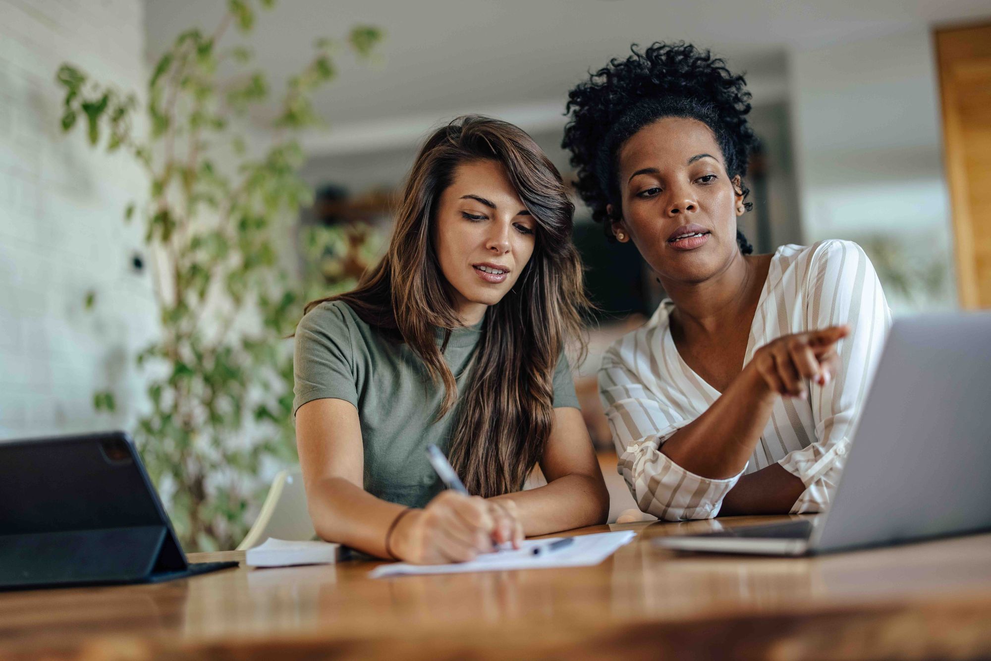 Two women planning at a table with paper, a computer, and a tablet