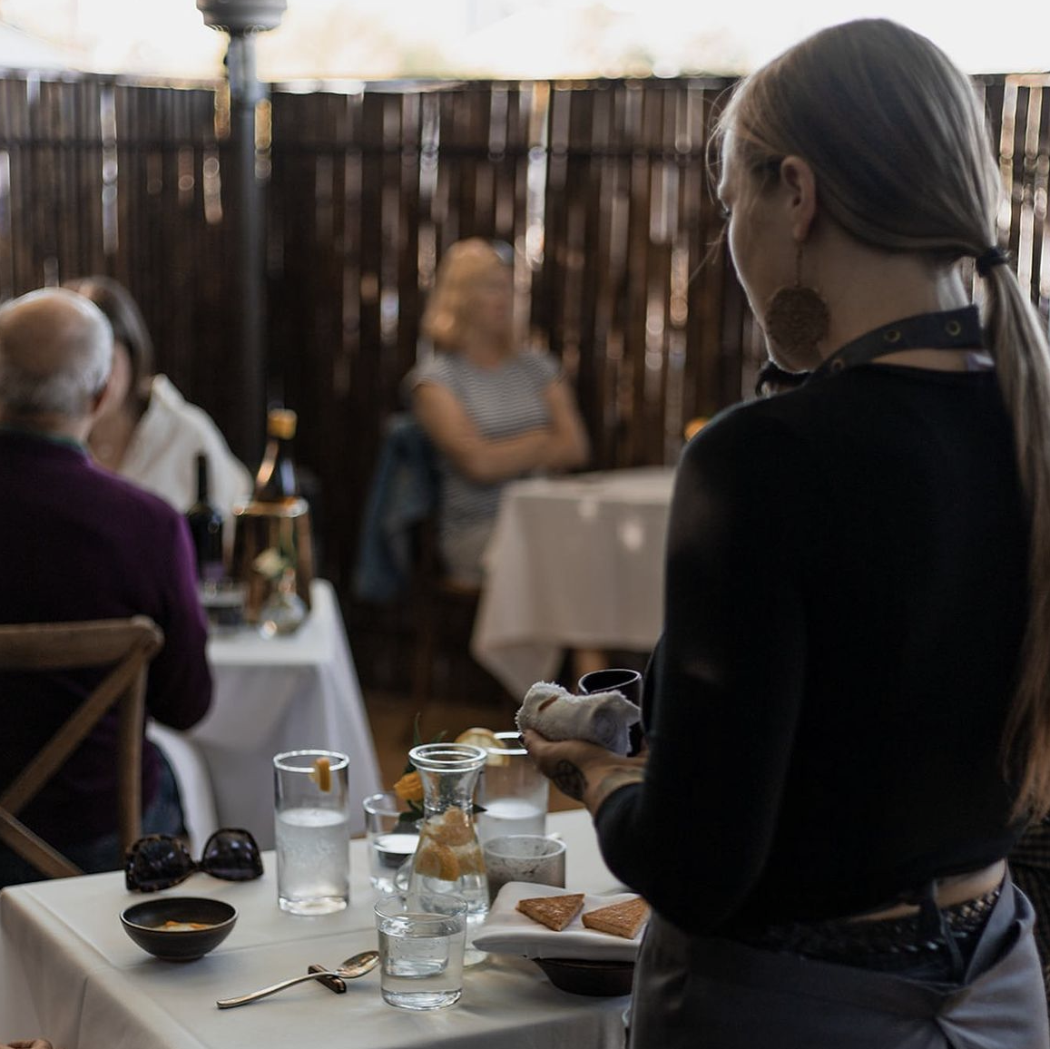 A server cleans a table on the patio at Table Culture Provisions