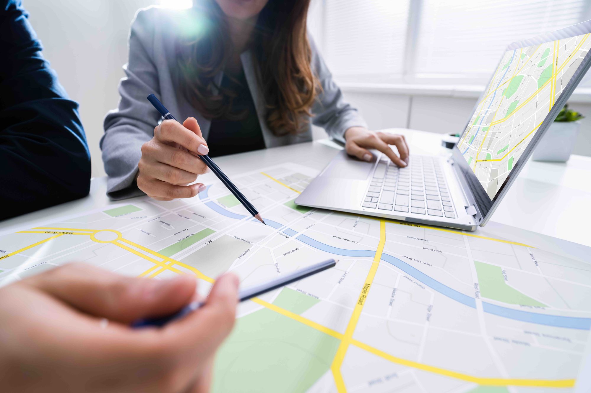 Two people studying an paper map along with a map on a computer.