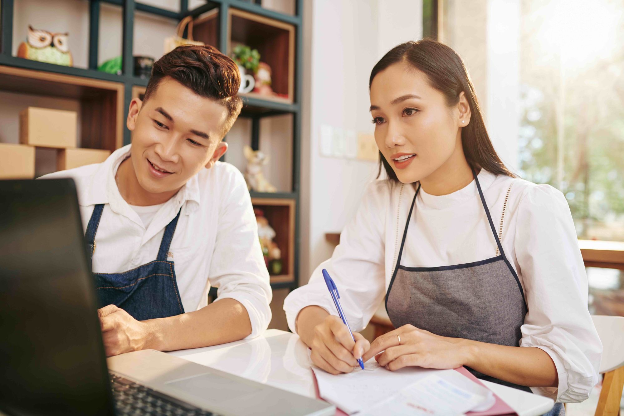 Young asian restaurant owners doing calculations on a computer.